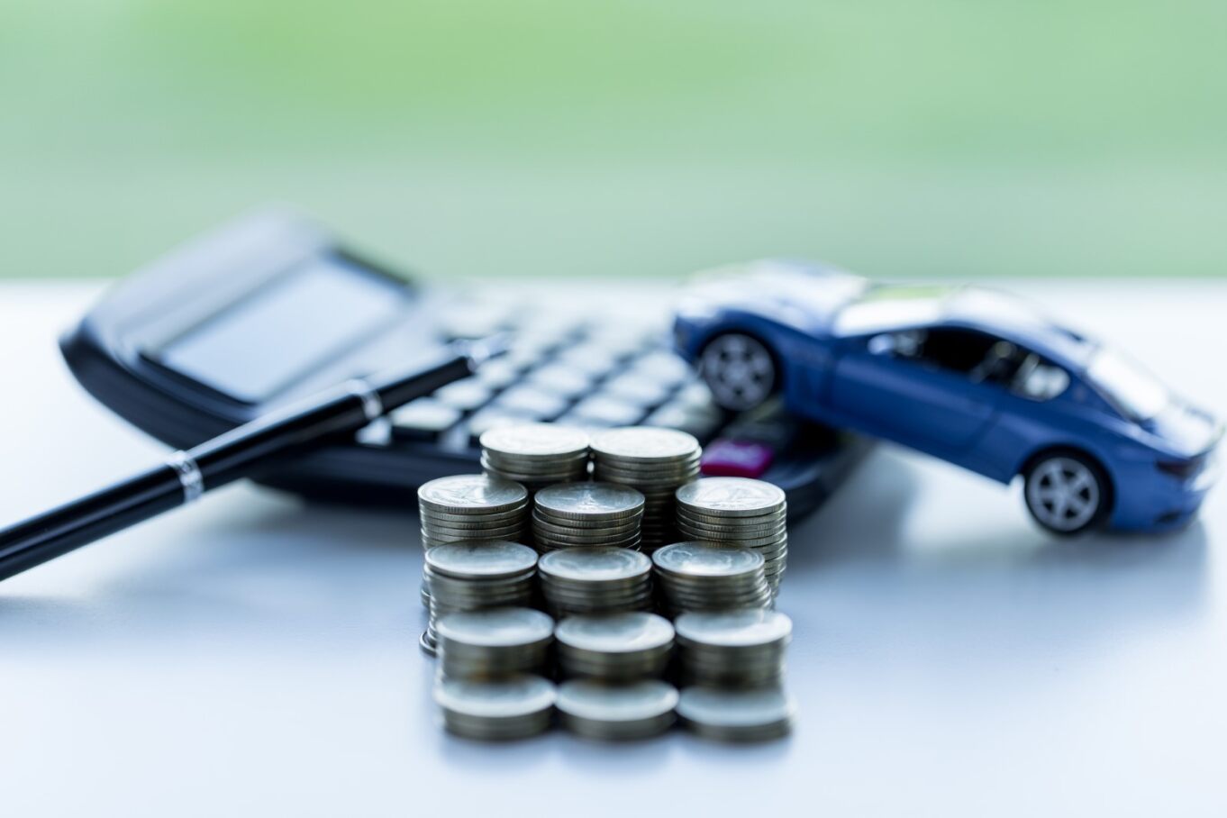 several stacks of coins, a calculator, a pen and a toy car